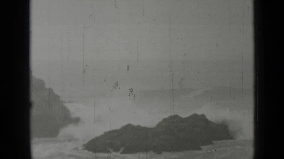1937 San Francisco coastal home-movie frame showing dark rocks, breaking surf, and a muted horizon in black-and-white 8mm film.