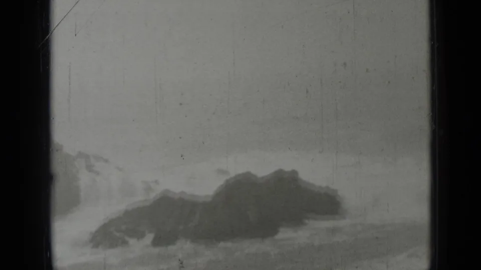1937 San Francisco coastal footage frame with dark rocks, white surf, and a hazy overcast horizon.