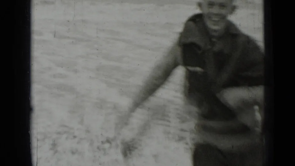 A boy plays near shallow surf in a soft, grainy 1937 San Francisco beach home movie frame.