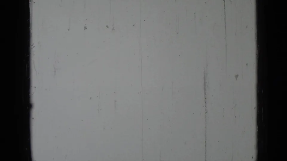 A blank or overexposed 8mm frame with visible scratches, dust, and a dark film border.