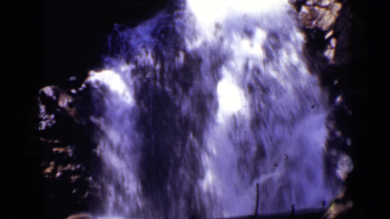 Rushing waterfall drops over dark rocks with bright white spray.