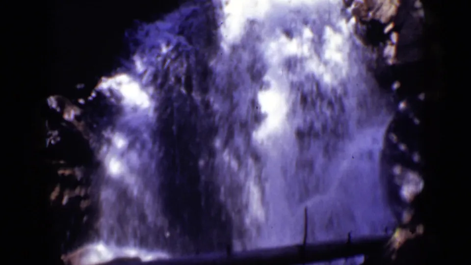 1938 Colorado 8mm frame showing rushing waterfall spray and dark rocky edges with a purple-blue film cast.