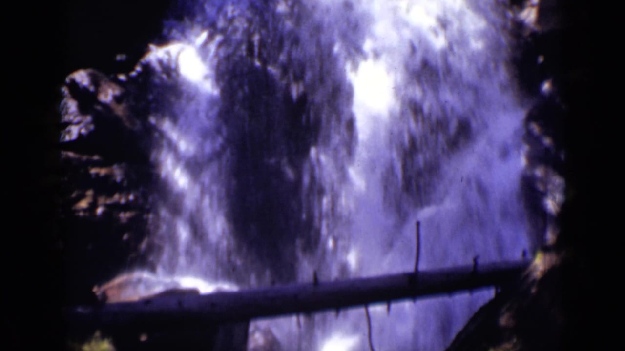 White water falls behind a dark horizontal log and jagged rock walls.