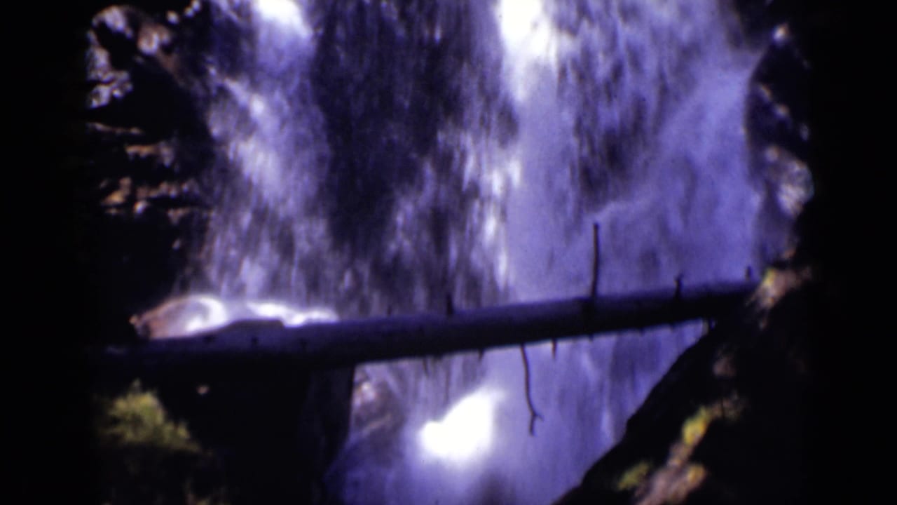 Rushing waterfall fills the frame behind a foreground log and dark rock.