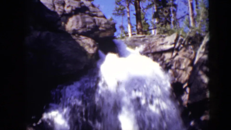 1938 Colorado 8mm frame of a white cascade dropping through rugged rock, with trees and sky above.