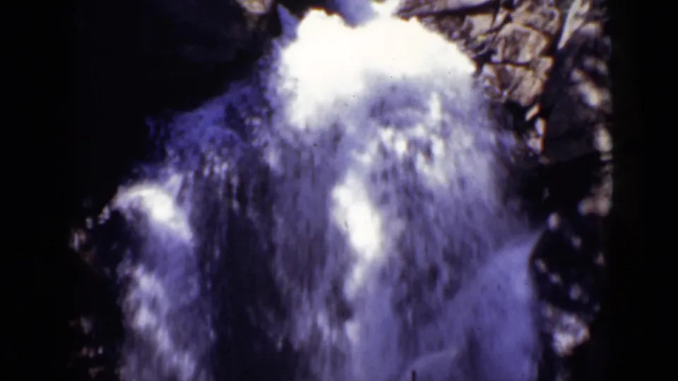 Close 8mm view of a Colorado waterfall with blown white spray and shadowed rock walls around the cascade.