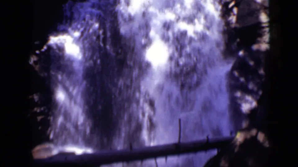 1938 Colorado 8mm frame showing a tall white cascade, dark stone, and a fallen log crossing the lower foreground.