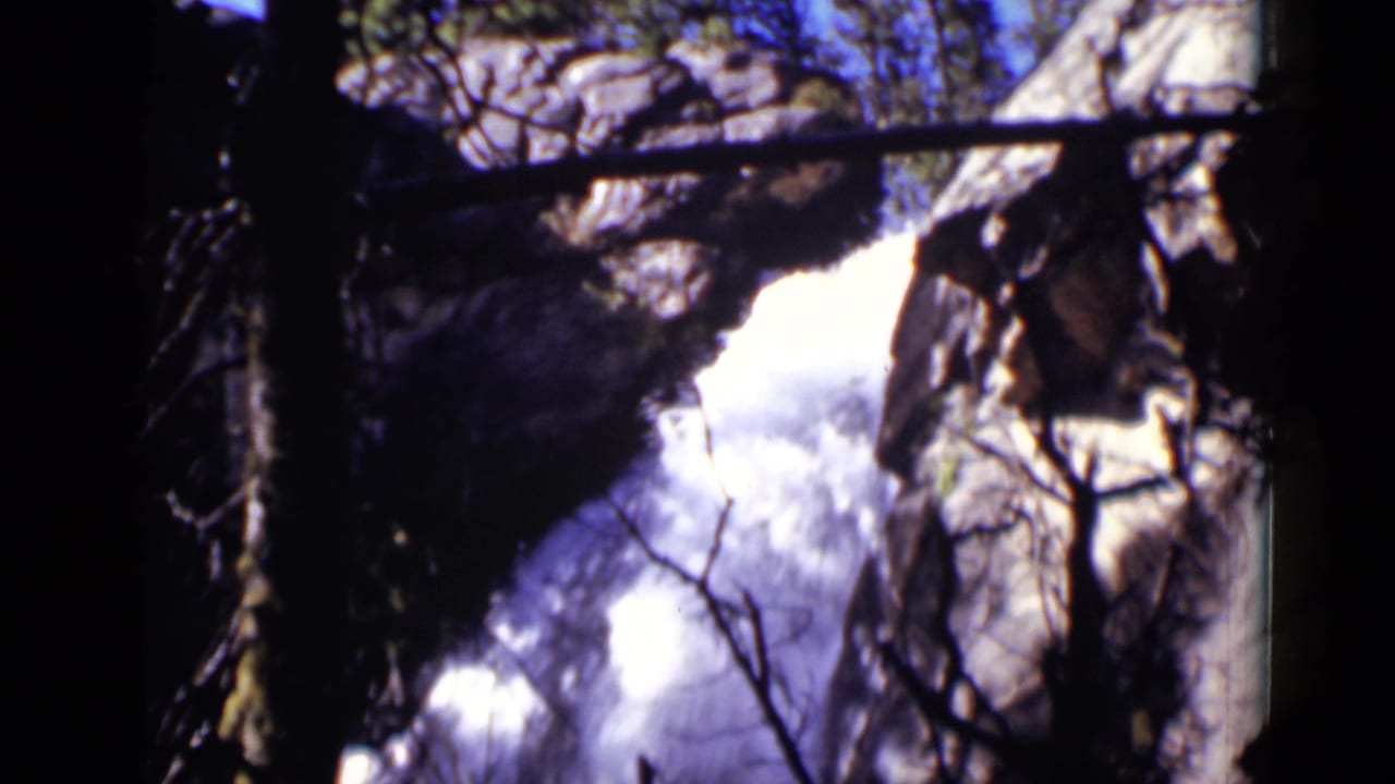 Waterfall rushing between rocky cliffs behind dark tree branches.