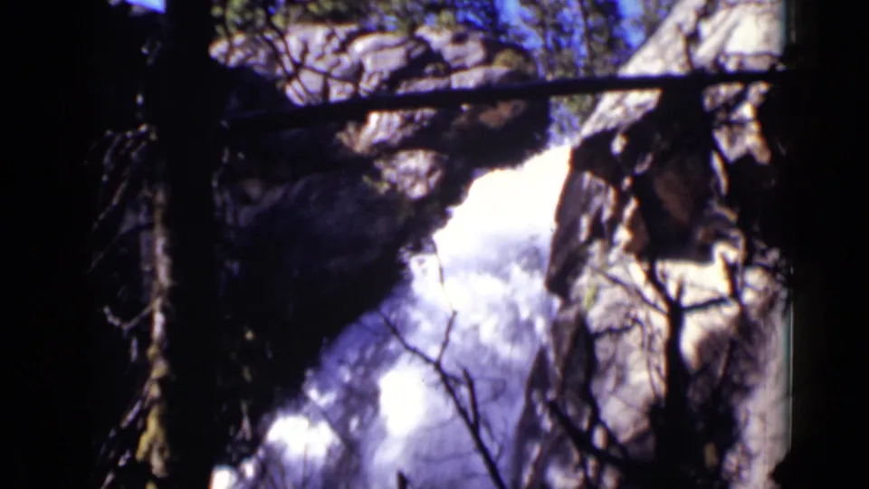 1938 Colorado 8mm frame showing a bright waterfall between rocks, partly obscured by silhouetted forest branches.