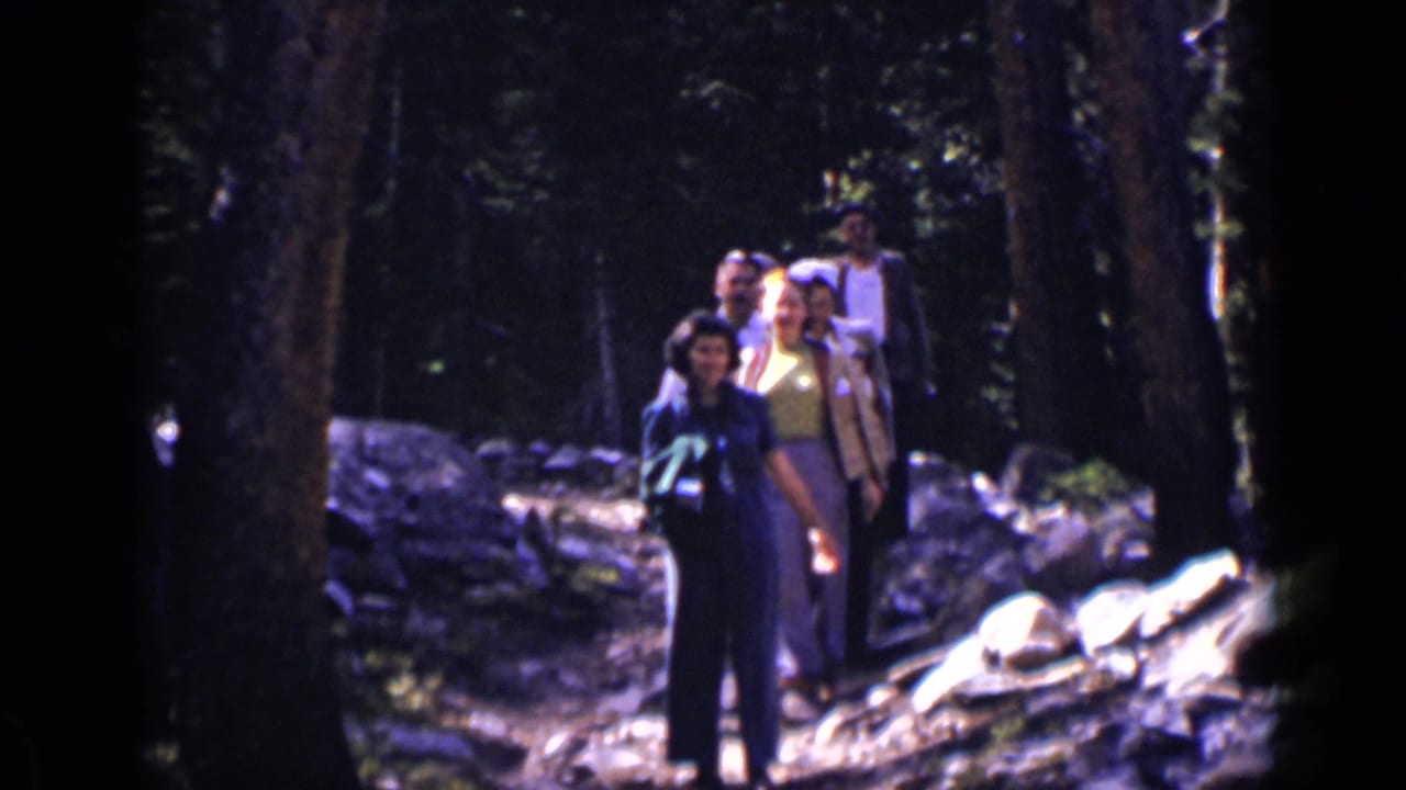 Several hikers on a wooded trail, with a woman in dark clothing near the front.