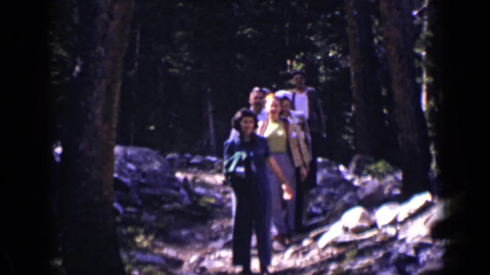 Adult hikers continue down a Colorado forest path in 1938 home-movie footage, with faces and period clothing visible.