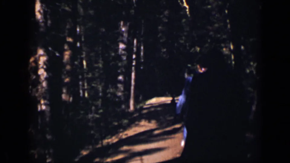 1938 Colorado 8mm frame with a blue-clad person seen from behind on a shaded dirt path in the woods.