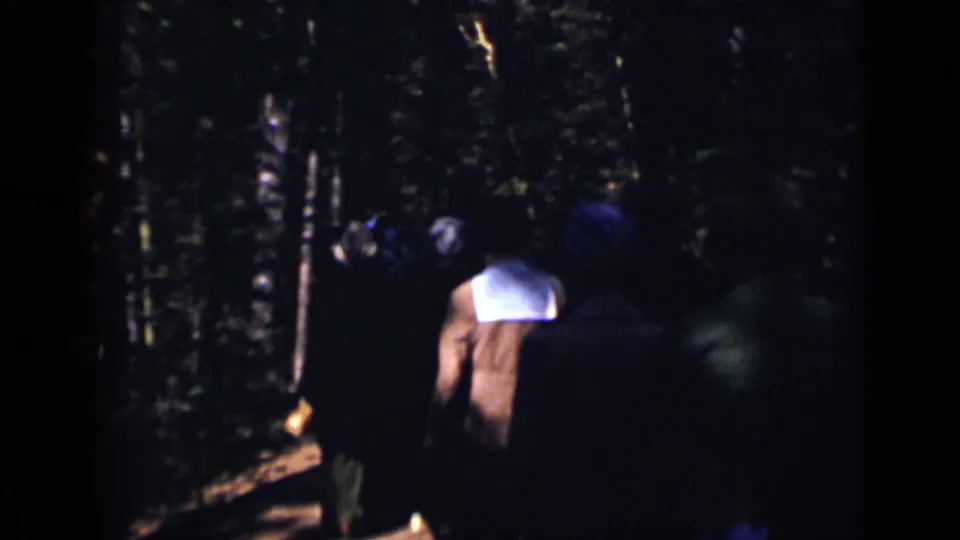 1938 Colorado 8mm frame showing several people walking away through a shadowed forest path.
