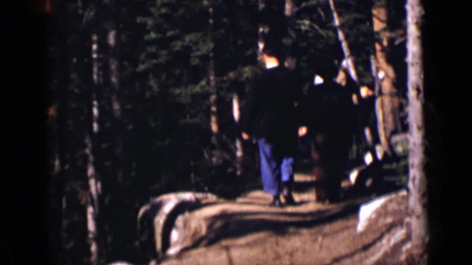 Adults on a wooded Colorado trail, seen from behind and partly obscured by shadow in 1938 home-movie footage.