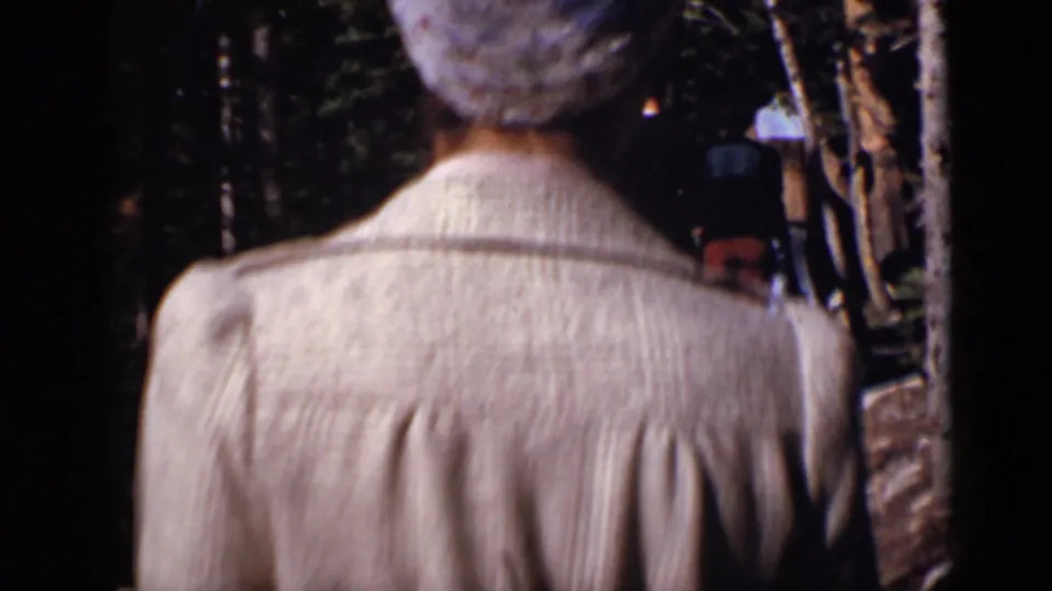 Rear view of a person in a light jacket following others along a shaded Colorado forest trail in 1938 footage.