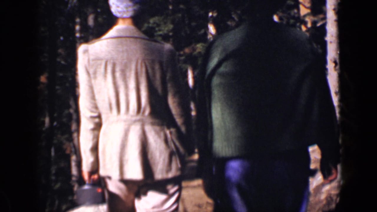 In Colorado 1938 home-movie footage, two adults walk away from the camera along a shaded forest path.