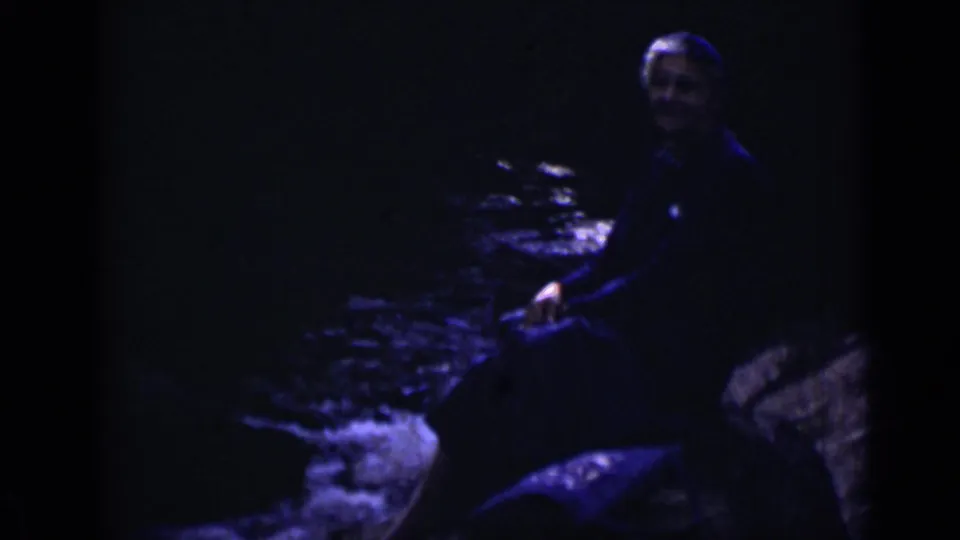 1938 Colorado 8mm frame with an adult seated on a sloped rock near a dark, fast-moving stream.