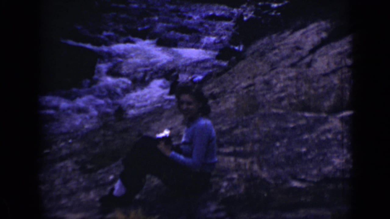 Person seated on rocks beside rushing water in a dark 8mm frame.
