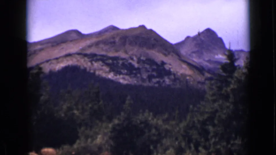 1938 Colorado 8mm frame showing rugged mountain ridges beyond evergreen forest, with dark film borders and soft focus.