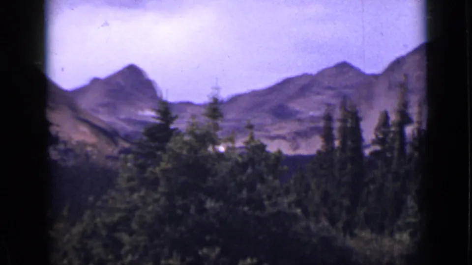 1938 Colorado home-movie view of mountain slopes and evergreen forest, softened by grain, color shift, and handheld framing.