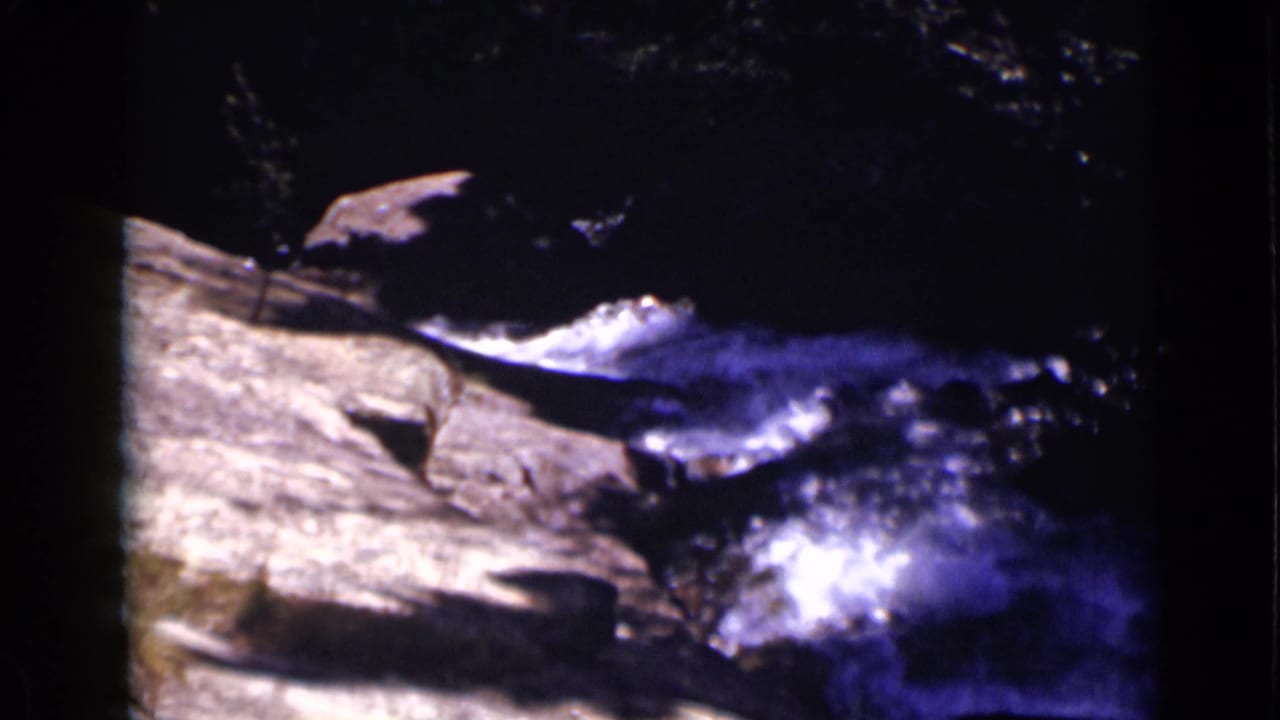 Rocky stream with fast water and bright reflections in a shaded setting.