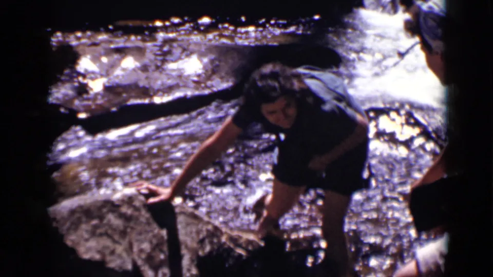 The person looks down and steadies themself on a rock as bright water flows across the rocky Colorado stream bed.