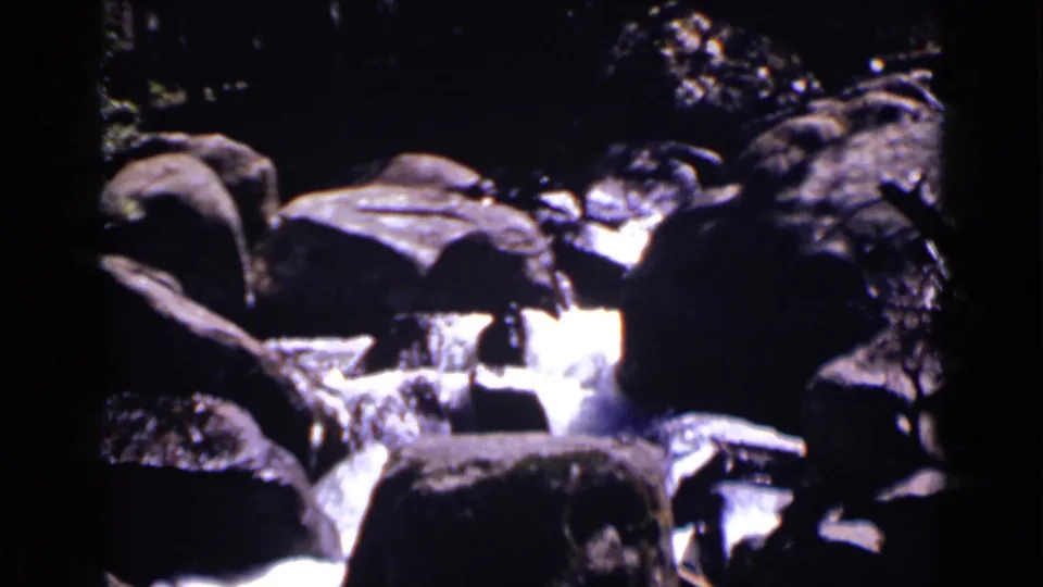 1938 Colorado 8mm frame showing white water cascading between dark boulders in forest shade.