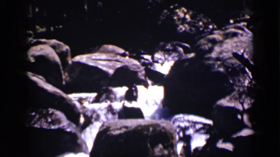 1938 Colorado home-movie view of Copeland Falls water flowing around large shaded rocks.