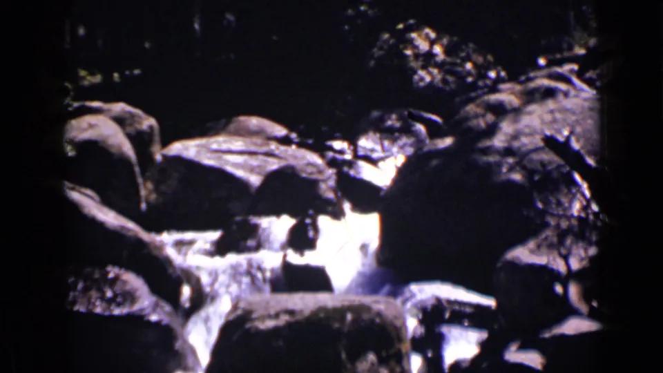 1938 Colorado 8mm frame of a rocky waterfall channel with bright water and dark foreground stones.