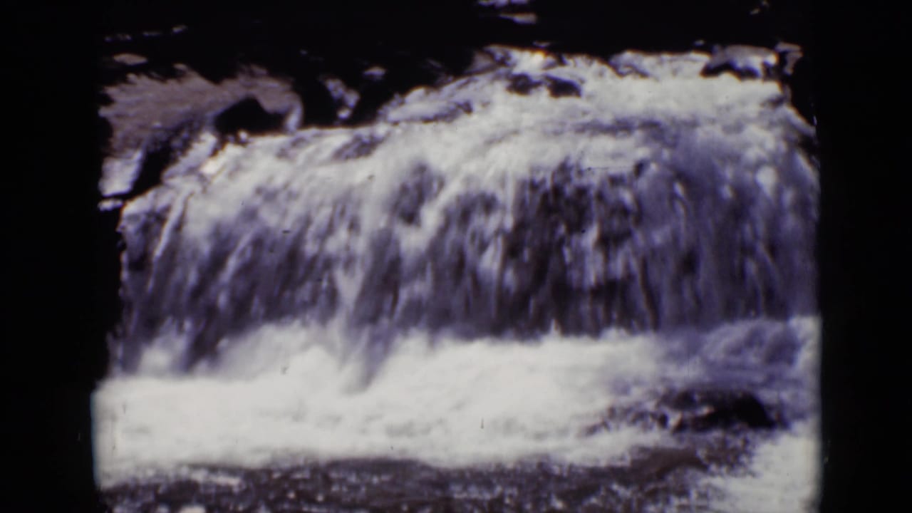 Small waterfall flowing over rocks with dark film borders and no clear person visible.
