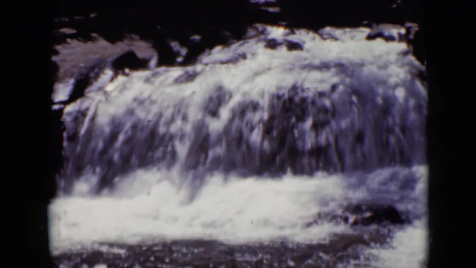 1938 Colorado 8mm frame showing a small waterfall spilling over rocks, with heavy shadowing and rounded film-frame edges.