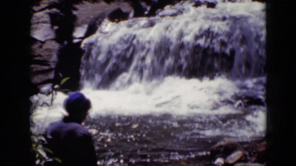 1938 Colorado 8mm frame with the woman partly in the foreground and the small waterfall and stream behind her.