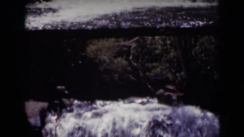 1938 Colorado 8mm frame showing the waterfall from a similar angle, with soft focus, dark foliage, wet rocks, and foamy water below.