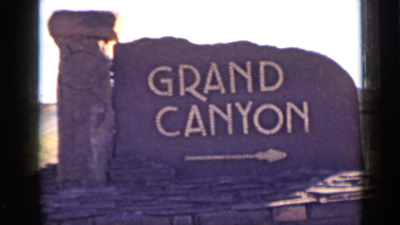 Grand Canyon stone sign with white lettering and an arrow, framed by dark film edges.