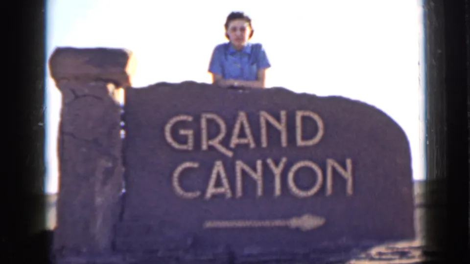 1939 Arizona home-movie frame showing a woman in a blue collared shirt posing behind the Grand Canyon sign.