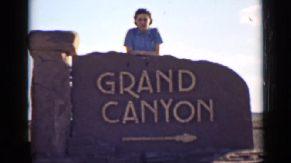 A 1939 8mm Arizona travel frame with a woman posing behind the Grand Canyon sign and leaning on the stone marker.
