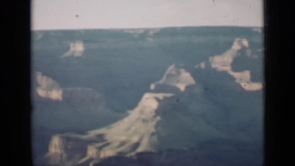 1939 Arizona travel-film frame showing a wide Grand Canyon view with light rock outcrops and deep blue haze.