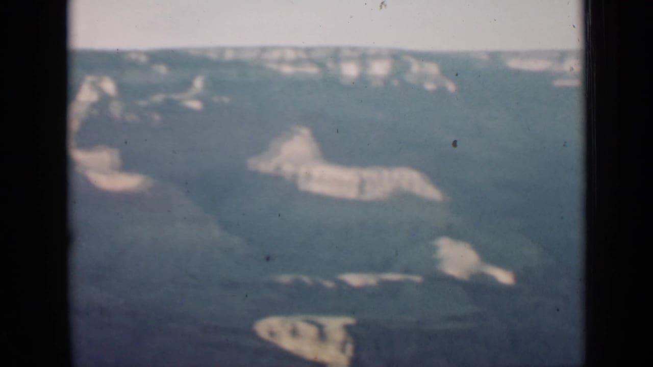 Soft 8mm view across Grand Canyon rock layers and shadowed ravines beneath a pale sky.