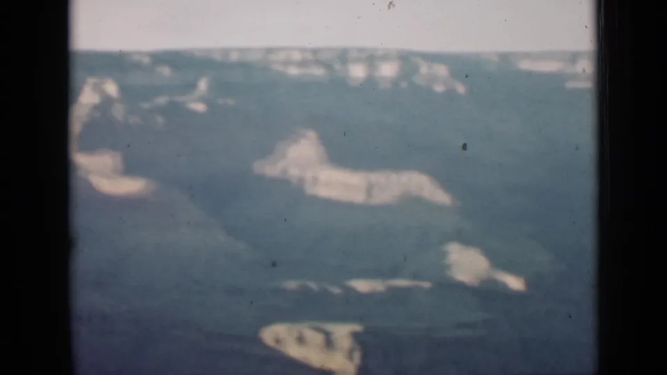 1939 Arizona home-movie frame showing a soft, distant view of Grand Canyon cliffs, layered rock, and dark ravines.