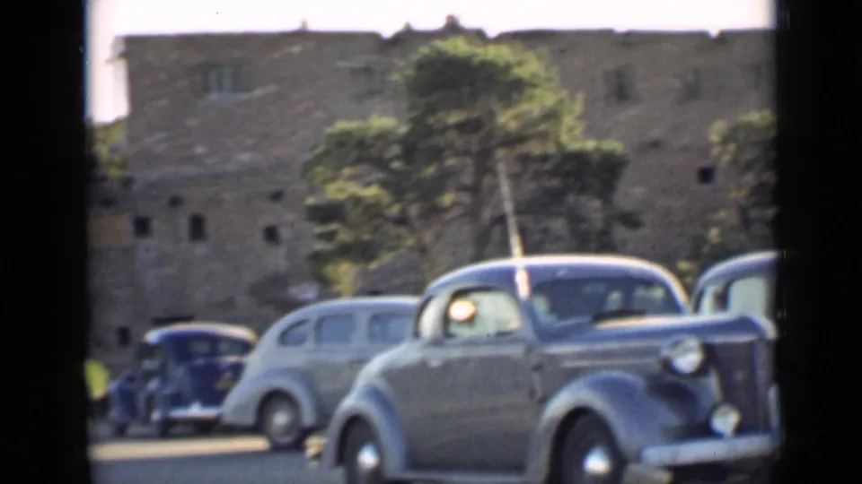 1939 Arizona home-movie view of several 1930s automobiles parked by a large stone building and trees.
