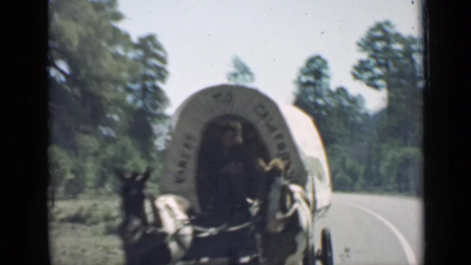 1939 Arizona frame showing a covered wagon attraction pulled by mules along a rural road with trees nearby.
