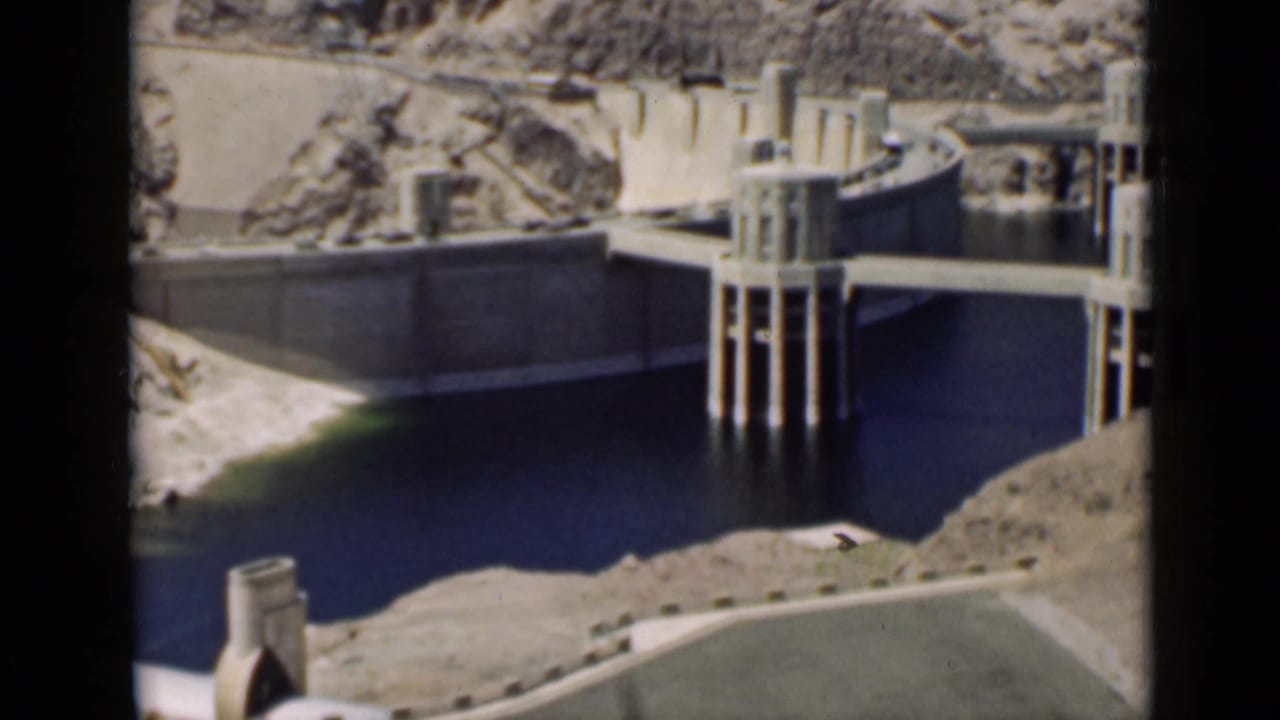 Concrete dam structure with reservoir water and rocky slopes.