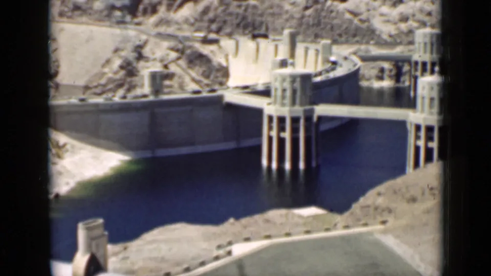 1939 Arizona home-movie frame of a dam complex with reservoir water, concrete supports, and arid surrounding slopes.