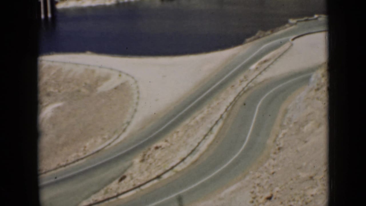 Winding paved road curves through pale rocky desert above reservoir water.