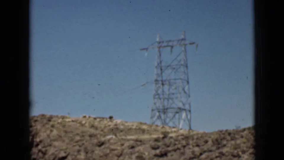 Steel power transmission tower on a desert ridge in Arizona, filmed in soft 8mm color against clear blue sky.