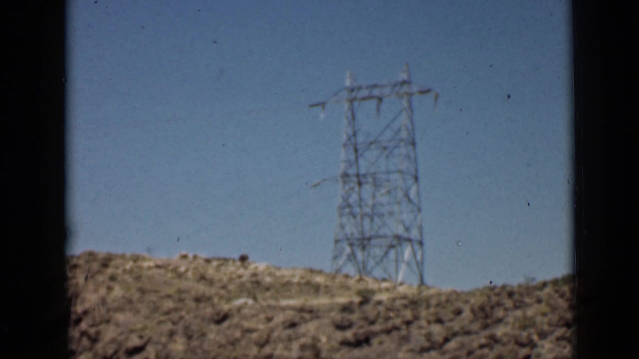 Steel electrical pylon on a rocky desert hill seen through dark window framing.