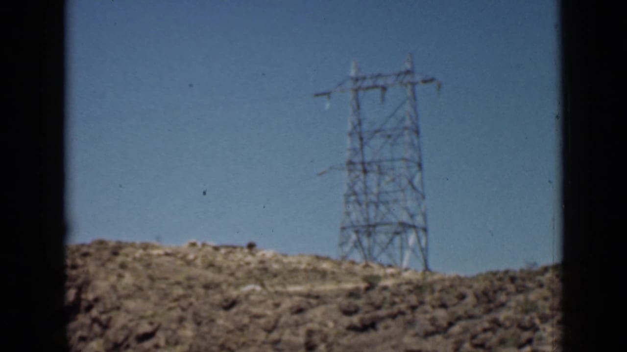 Electrical pylon on a desert hill with dark vertical window framing at the side.