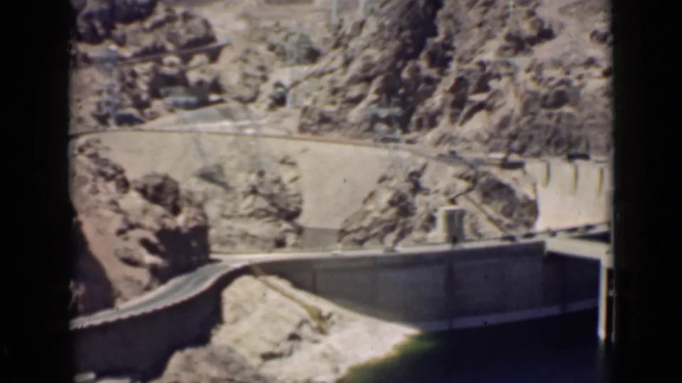A 1939 Arizona travel frame looks through a car window toward a concrete dam wall and canyon roadway.