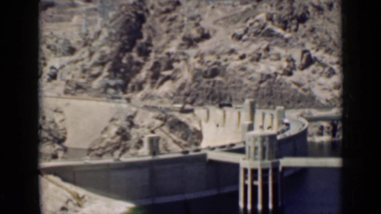 Dam wall, intake tower, water, and rocky hillside seen through 8mm frame edges.