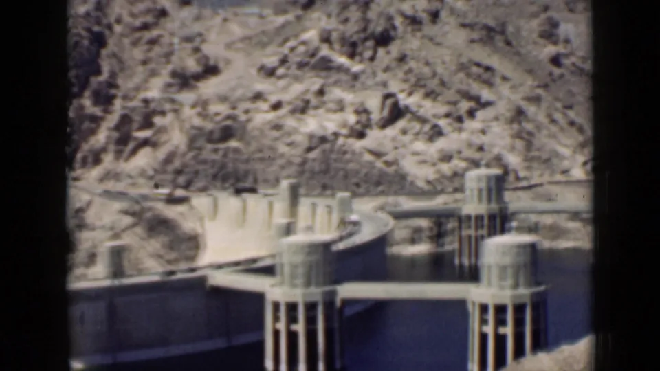Wide 1939 8mm view of Hoover Dam infrastructure, water, and rugged Arizona canyon terrain.